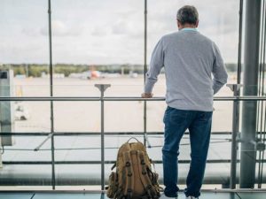 Locum tenens travel tips - Man standing inside airport looking outside of window at airplane