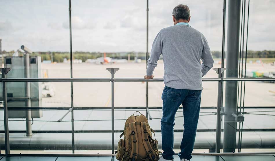 Locum tenens travel tips - Man standing inside airport looking outside of window at airplane