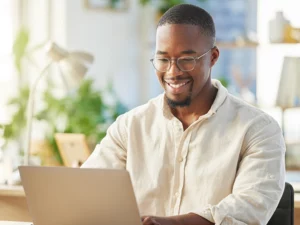 Man looking at a laptop while smiling in a sunny room