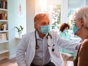 Older physician caring for a patient while another healthcare worker sits in the background
