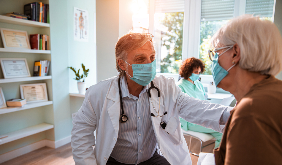 Older physician caring for a patient while another healthcare worker sits in the background