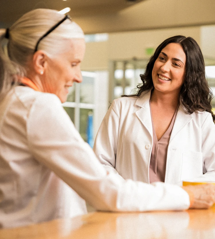 Two locums physicians smile and chat with each other in the workplace.